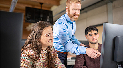 Professor erklärt Studierenden etwas am PC