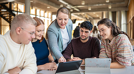 Prof. Dr. Wibke Heidig erklärt Studierenden im Foyer etwas am Tablet