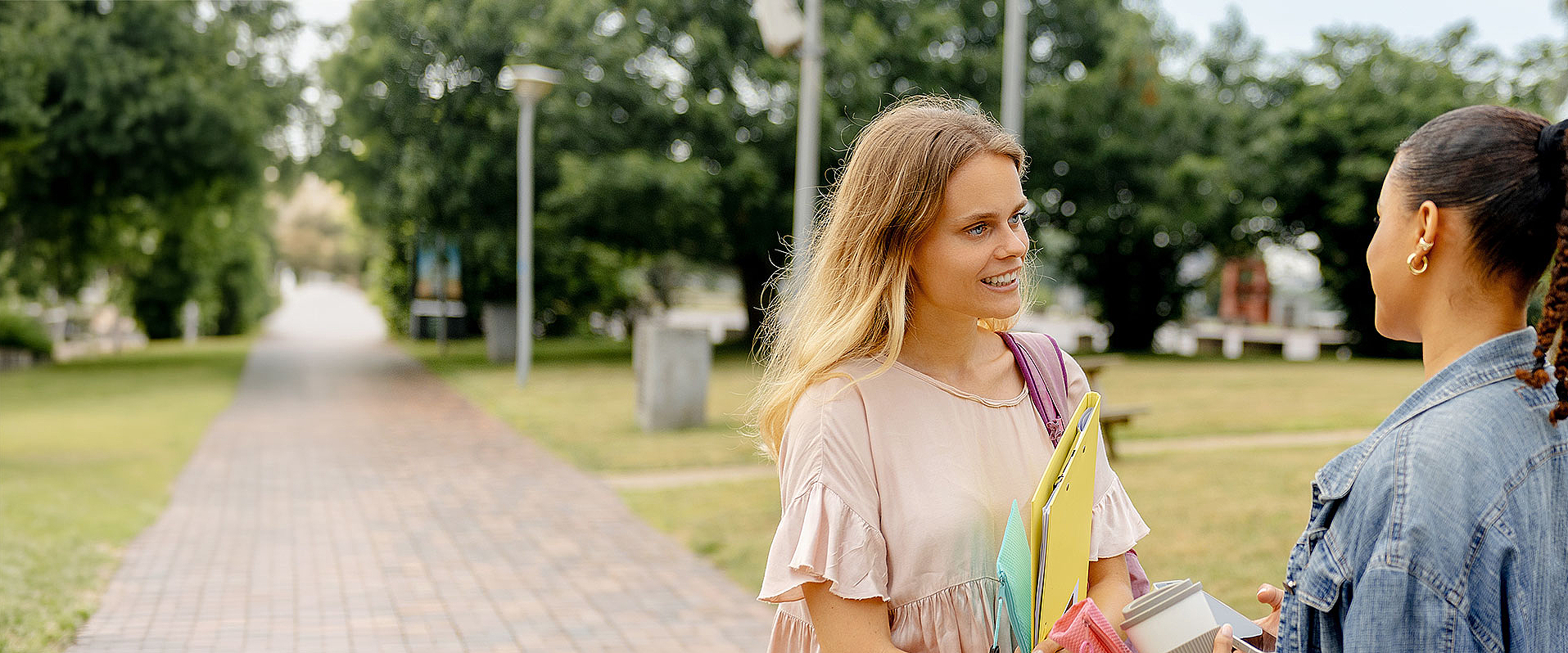 Zwei junge Studentinnen begegnen sich auf dem Campus und unterhalten sich.