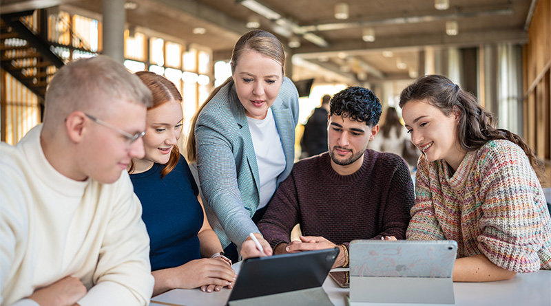 Prof. Dr. Wibke Heidig erklärt Studierenden im Foyer etwas am Tablet