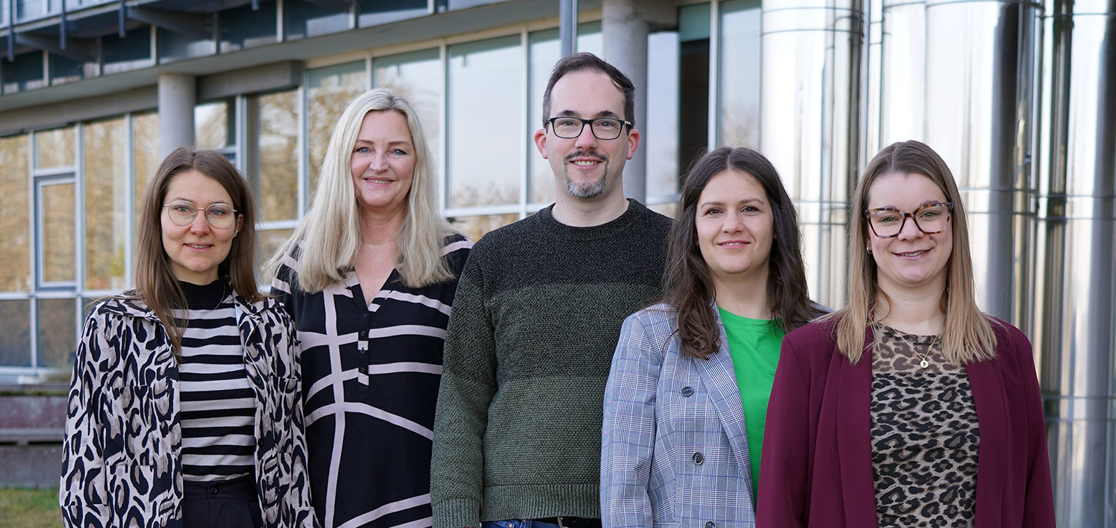 Fünf Mitglieder des Personalrats stehen nebeneinander vor einem Hochschulgebäude und blicken in die Kamera